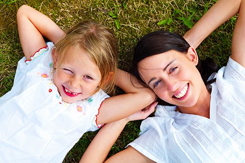 mother and child smiling whilst laying down on the grass